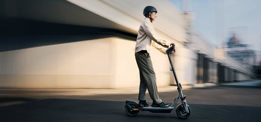 Helmeted rider using a Segway Ninebot F3 electric scooter beside modern buildings
