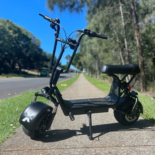 Kush Mini Steezer X seated electric scooter parked on a tree-lined path.