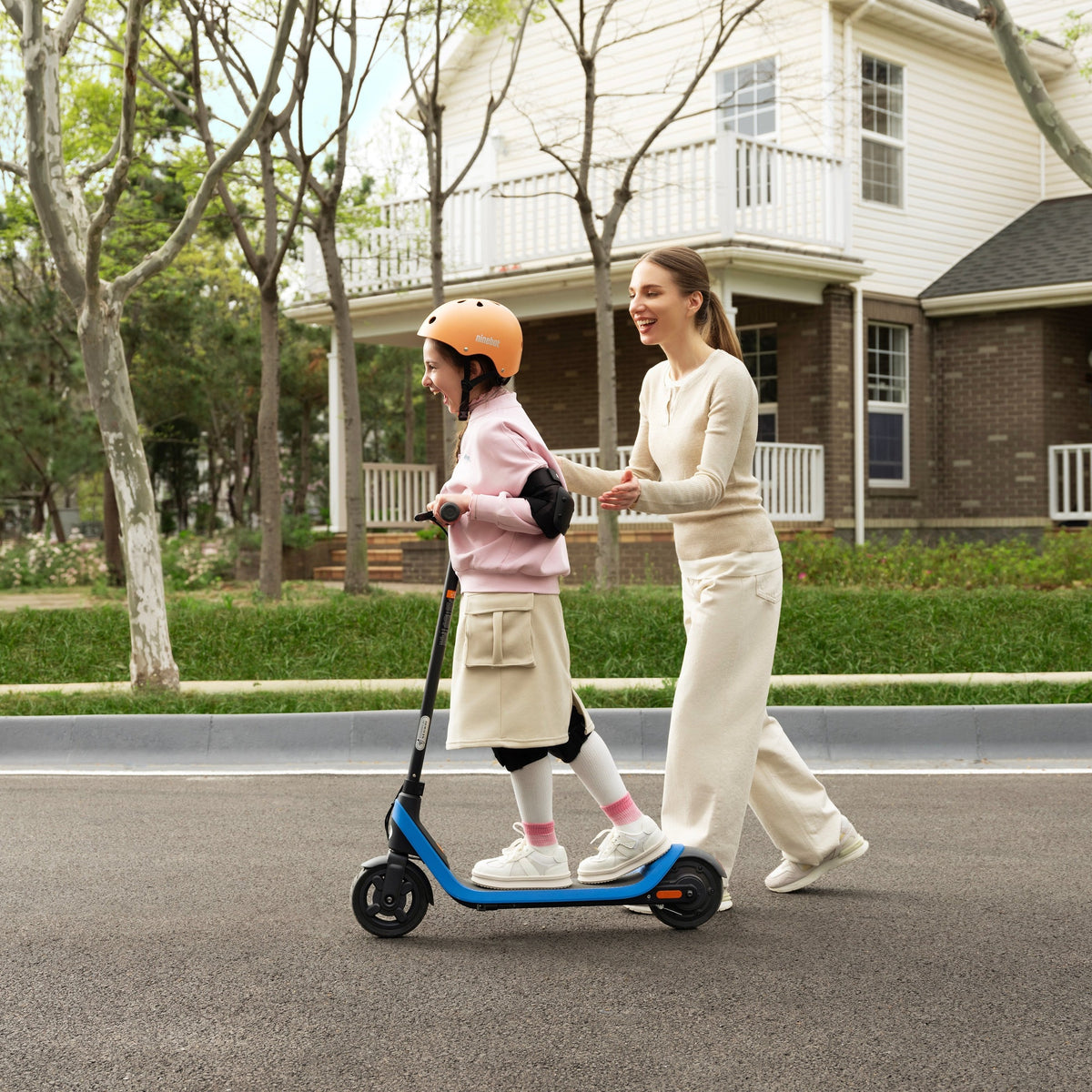 Helmeted child with a blue Segway Ninebot C2 Lite electric scooter beside a parent outdoors.