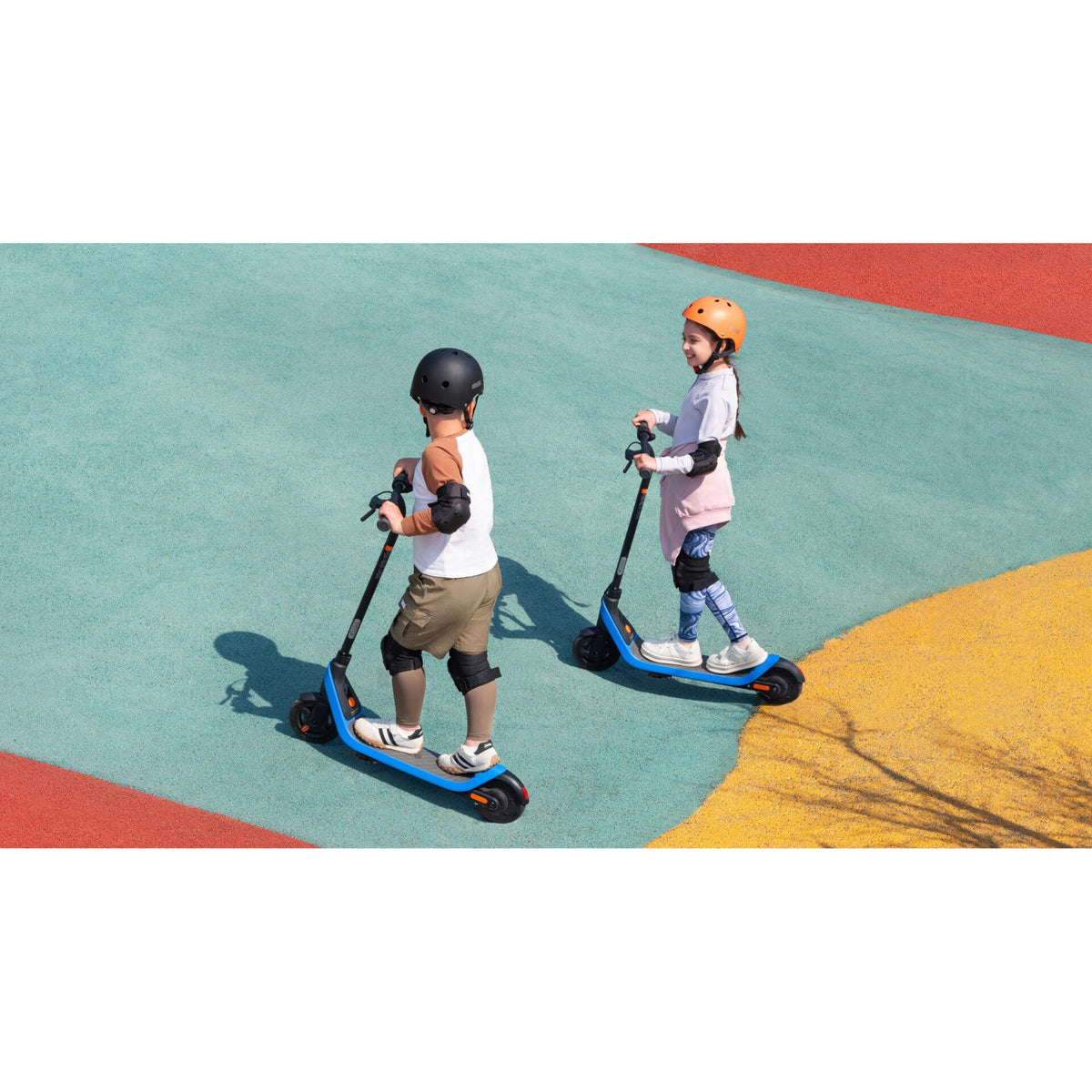 Two helmeted children riding blue Segway Ninebot C2 Lite scooters on a colourful paved surface.