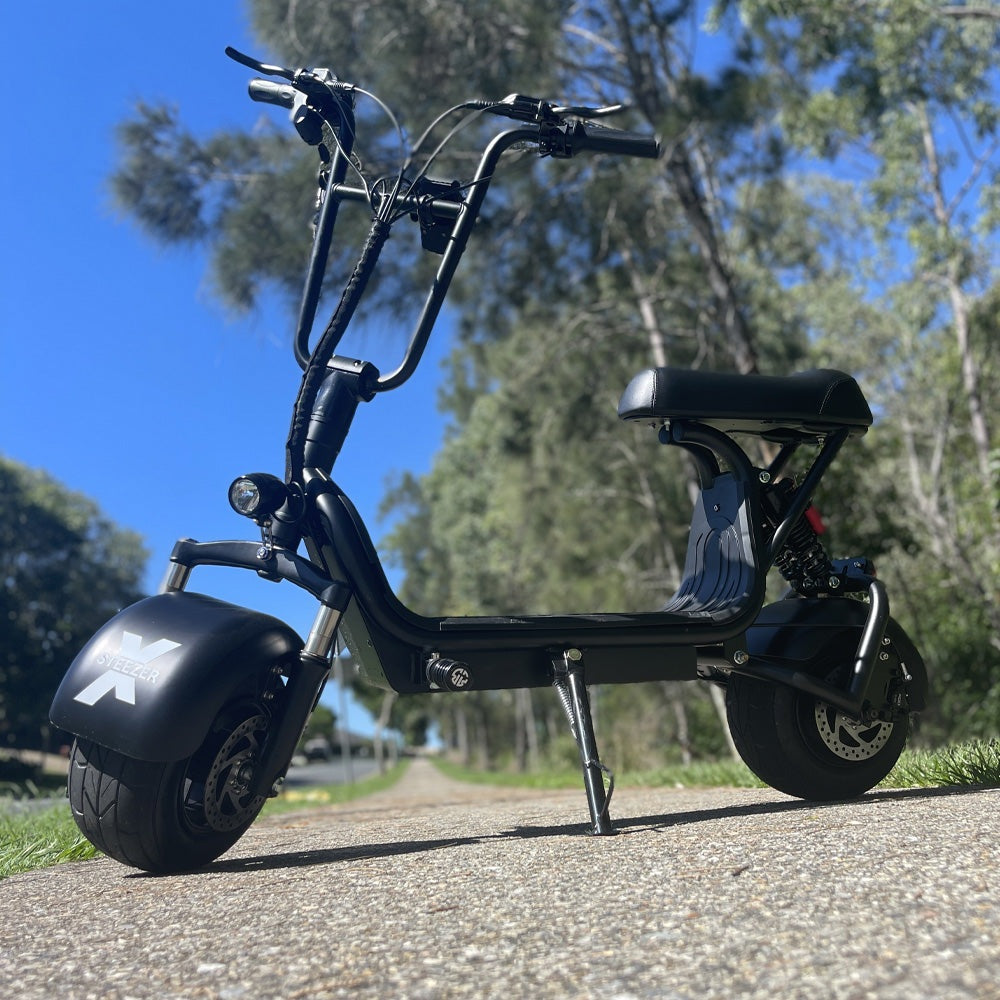 Kush Mini Steezer X seated electric scooter parked beside a tree-lined path.