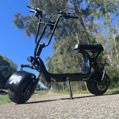 Kush Mini Steezer X seated electric scooter parked beside a tree-lined path.