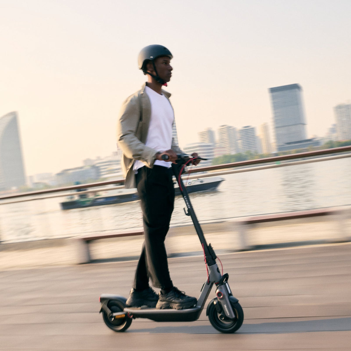 Helmeted rider using a Segway F3 Pro electric scooter beside the waterfront